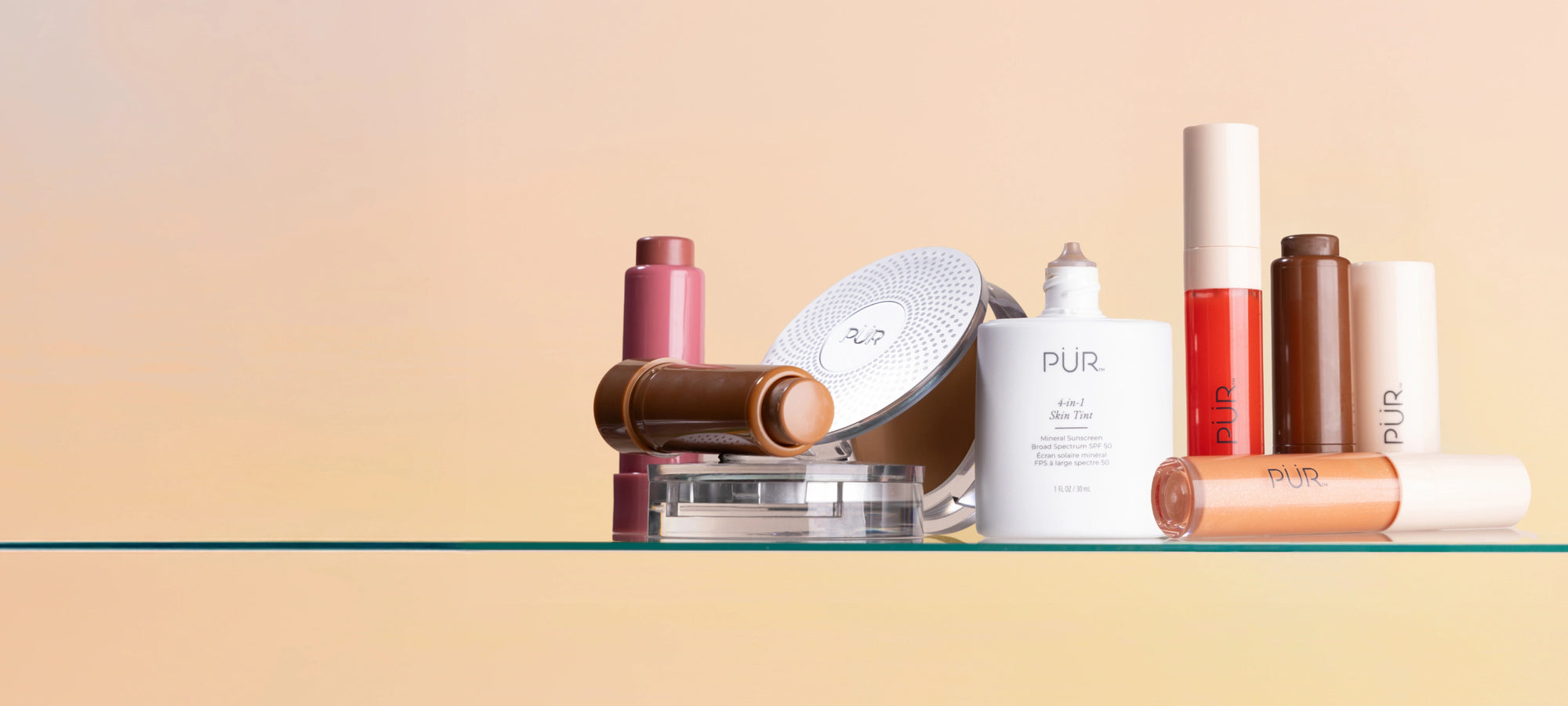 Memorial Day - 30% Off Sitewide: Various PÜR makeup and complexion products stacked on glass surface against pink-to-yellow gradient background (desktop)