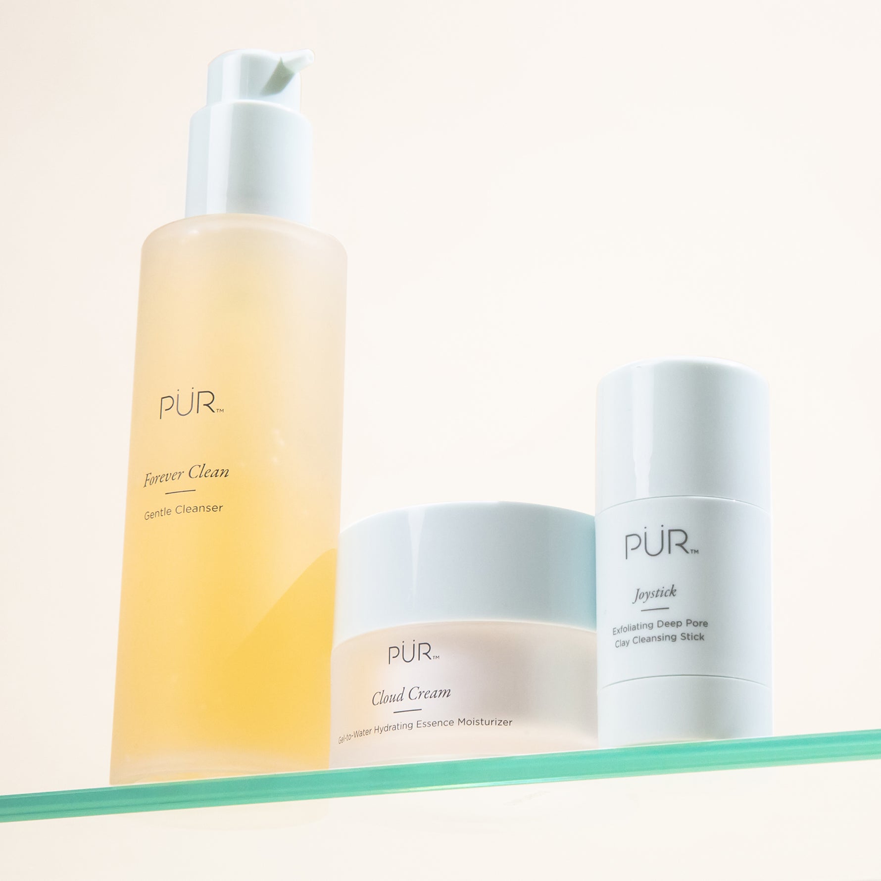 PÜR skincare trio on a glass shelf featuring Forever Clean Cleanser, Cloud Cream Moisturizer, and Joystick Exfoliating Cleansing Stick.