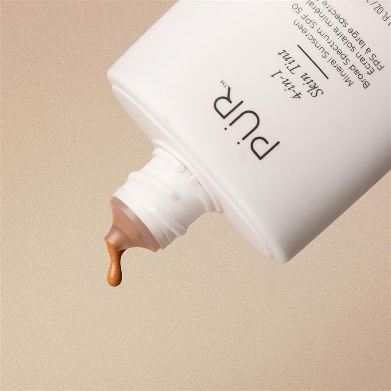 White bottle with brown liquid being squeezed out on a beige background